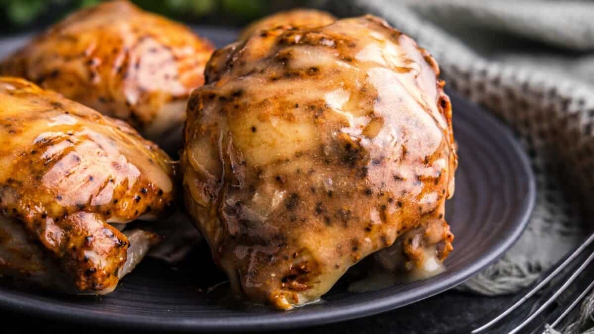 A close up view of a chicken thigh with an apple cider glaze on a black plate.