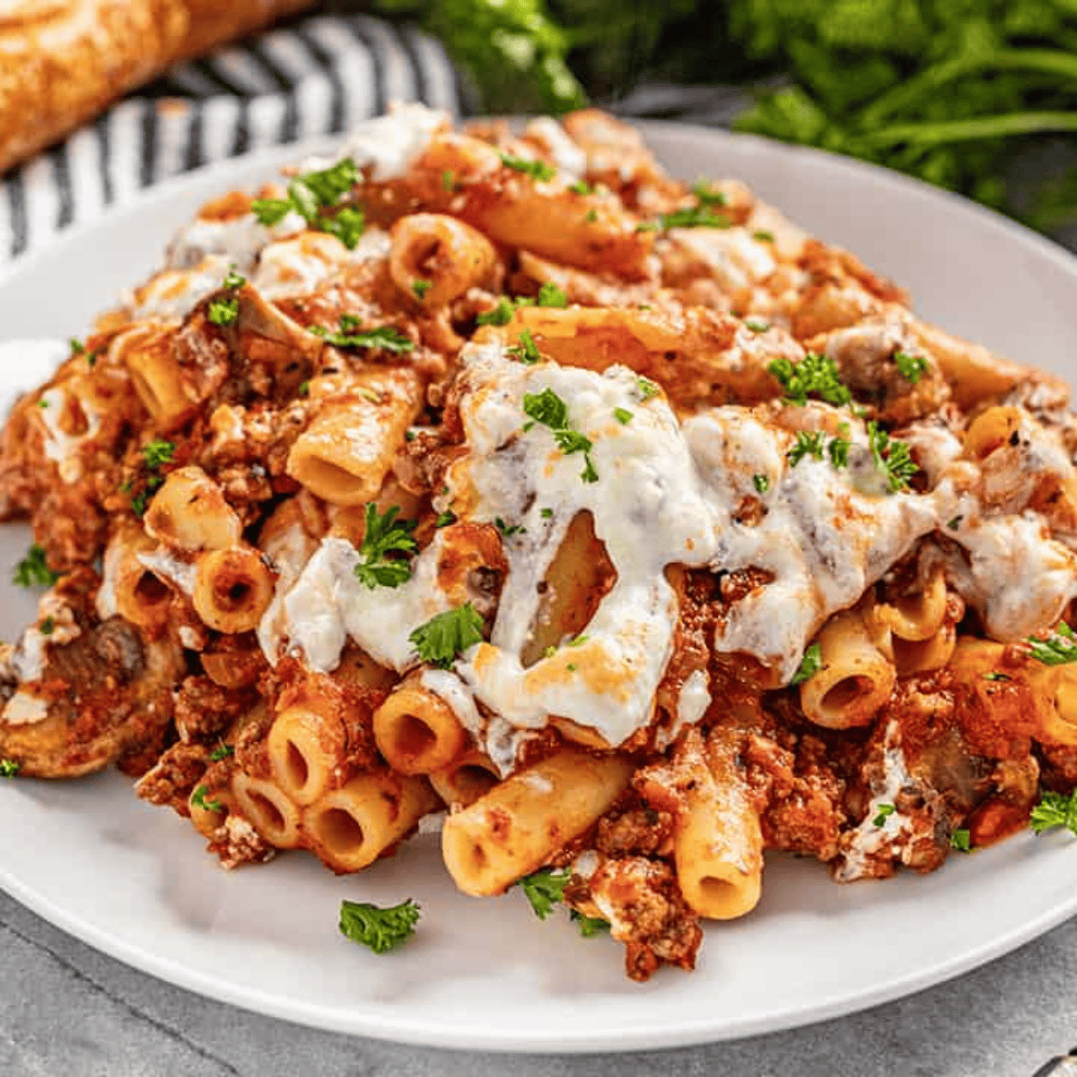 A large serving of baked ziti sprinkled with parsley on a white plate.