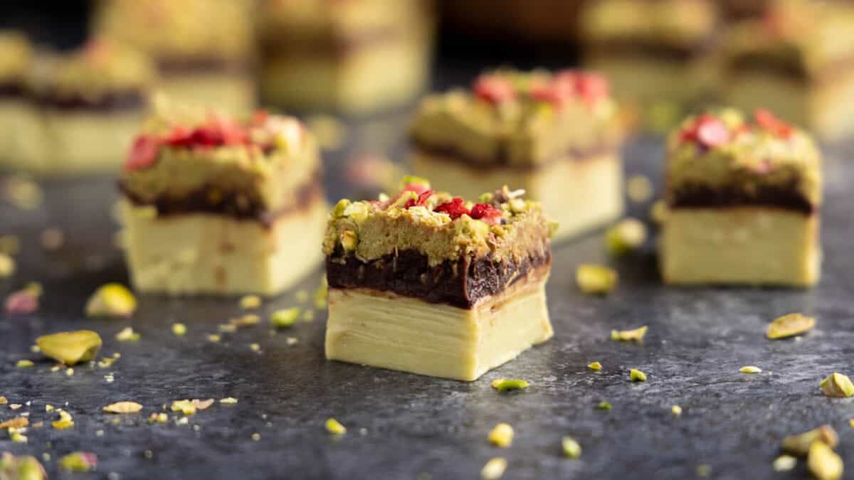 A closeup view of a piece of Dubai Chocolate Fudge with a pistachio base, chocolate ganache layer, and a kataifi topping.