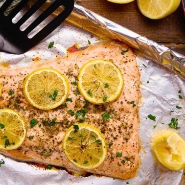 Easy Garlic Herb Baked Salmon topped with lemons on a sheet pan.
