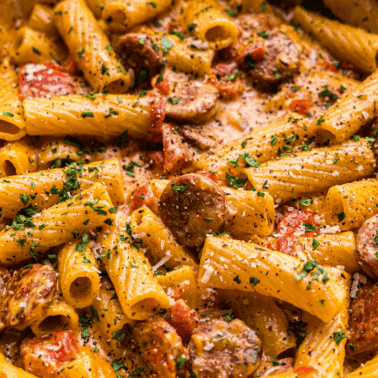 A closeup view into a pot of creamy cajun sausage pasta with coins of andouille sausage.