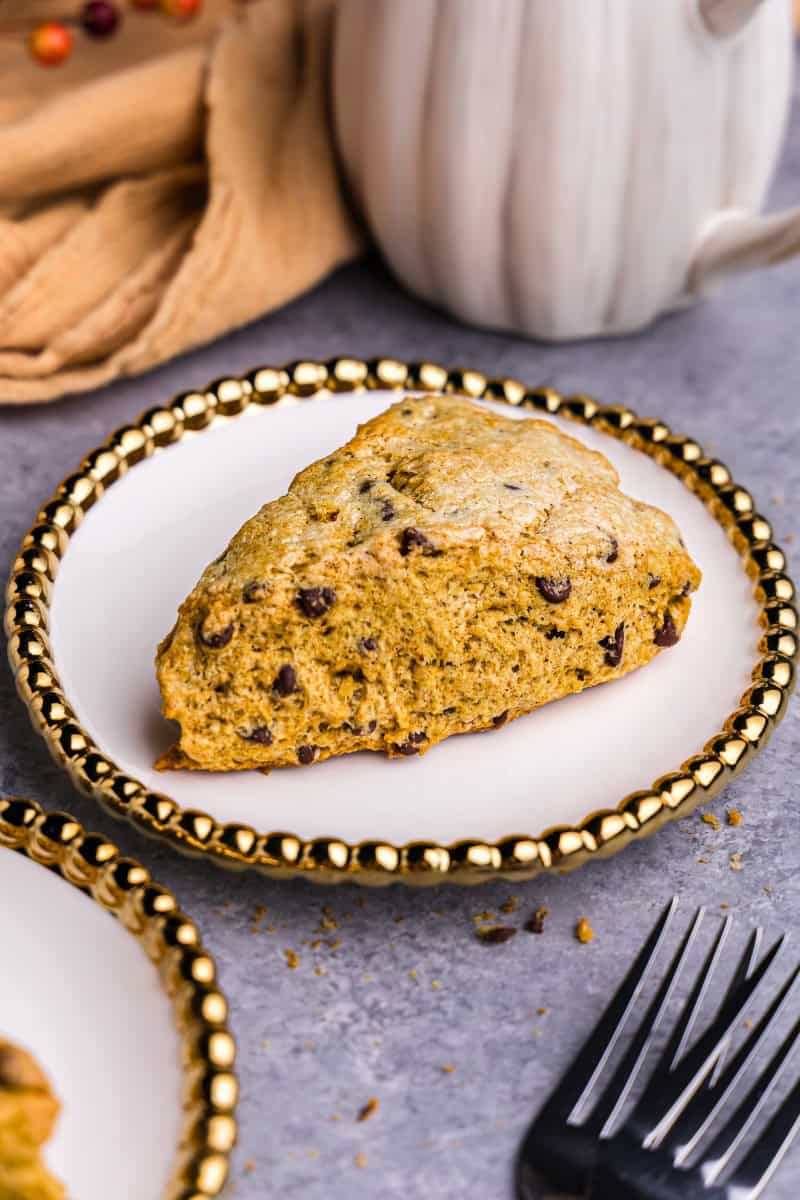 A single wedge-shaped pumpkin chocolate chip scone on a white plates with a beaded gold rim.