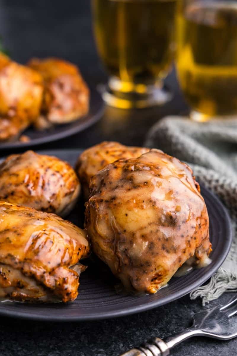 Apple cider glazed chicken thighs on a black plate with mugs of apple cider in the background.