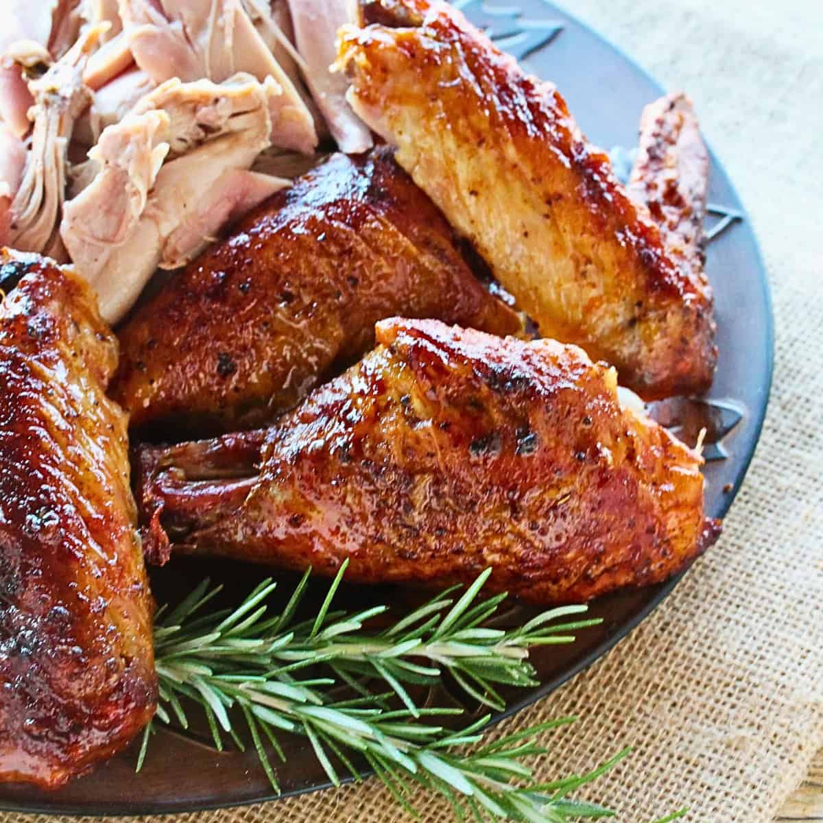 Carved pieces of a juicy roasted turkey on a serving platter with sprigs of rosemary.