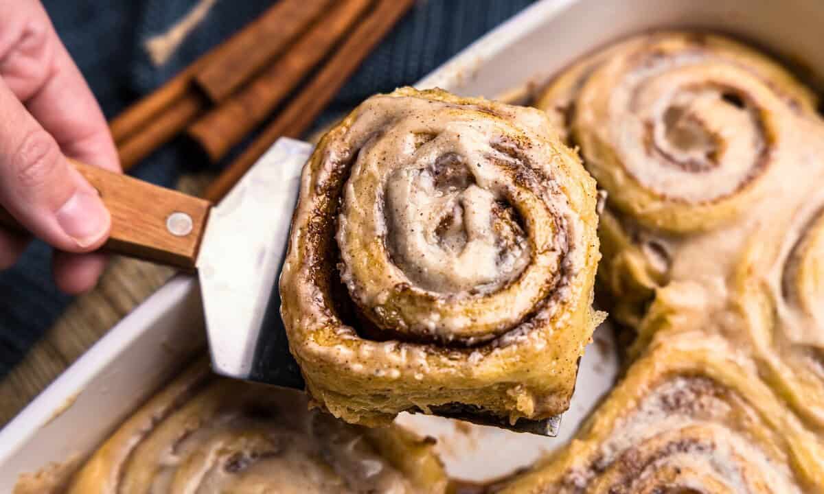 A chai latte sweet roll being lifted out of the pan with a spatula.