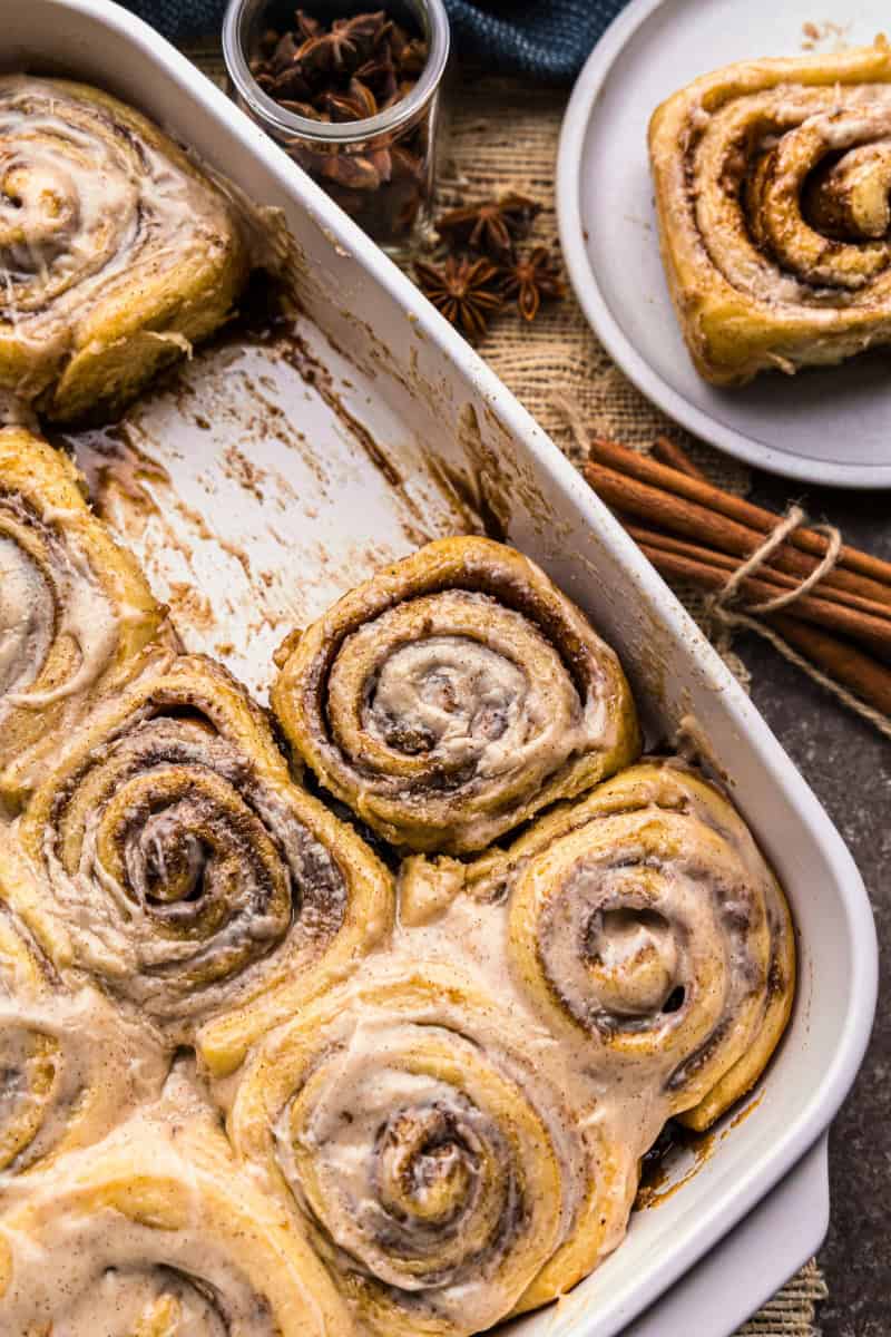 An overhead view of a pan of chai latte cinnamon rolls. One sweet roll has been removed and is sitting on a plate for serving.