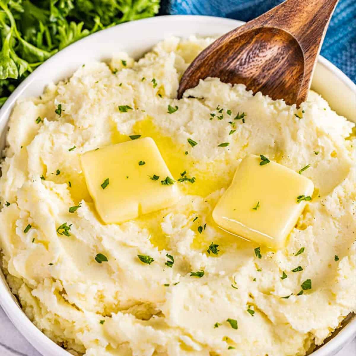A bowl of creamy mashed potatoes. Two pats of butter are melting on top, oozing into the fluffy potatoes.
