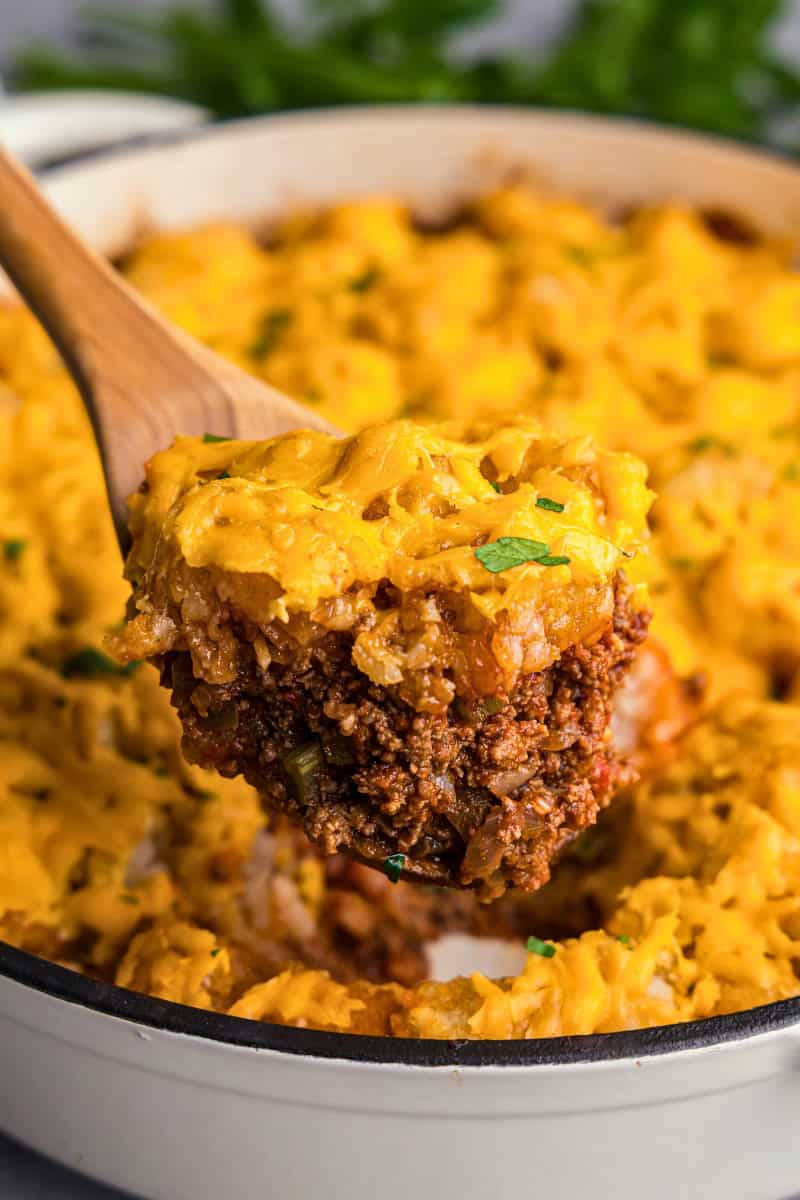 A close up view of a large spoonful of tater tot casserole being dished up from the pan.