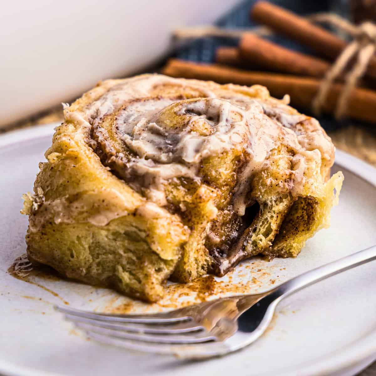 A chai latte cinnamon roll on a white plate. A bite has been taken out revealing the gooey chai filling. A fork is resting on the plate.